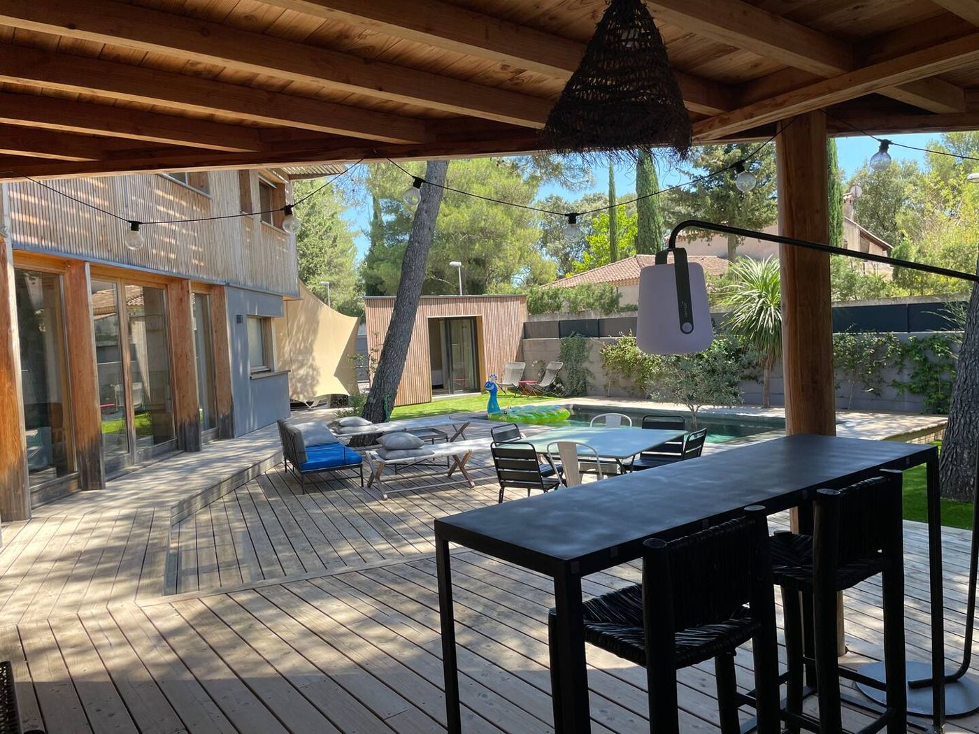 La terrasse couverte, ses guirlandes et la vue sur la piscine